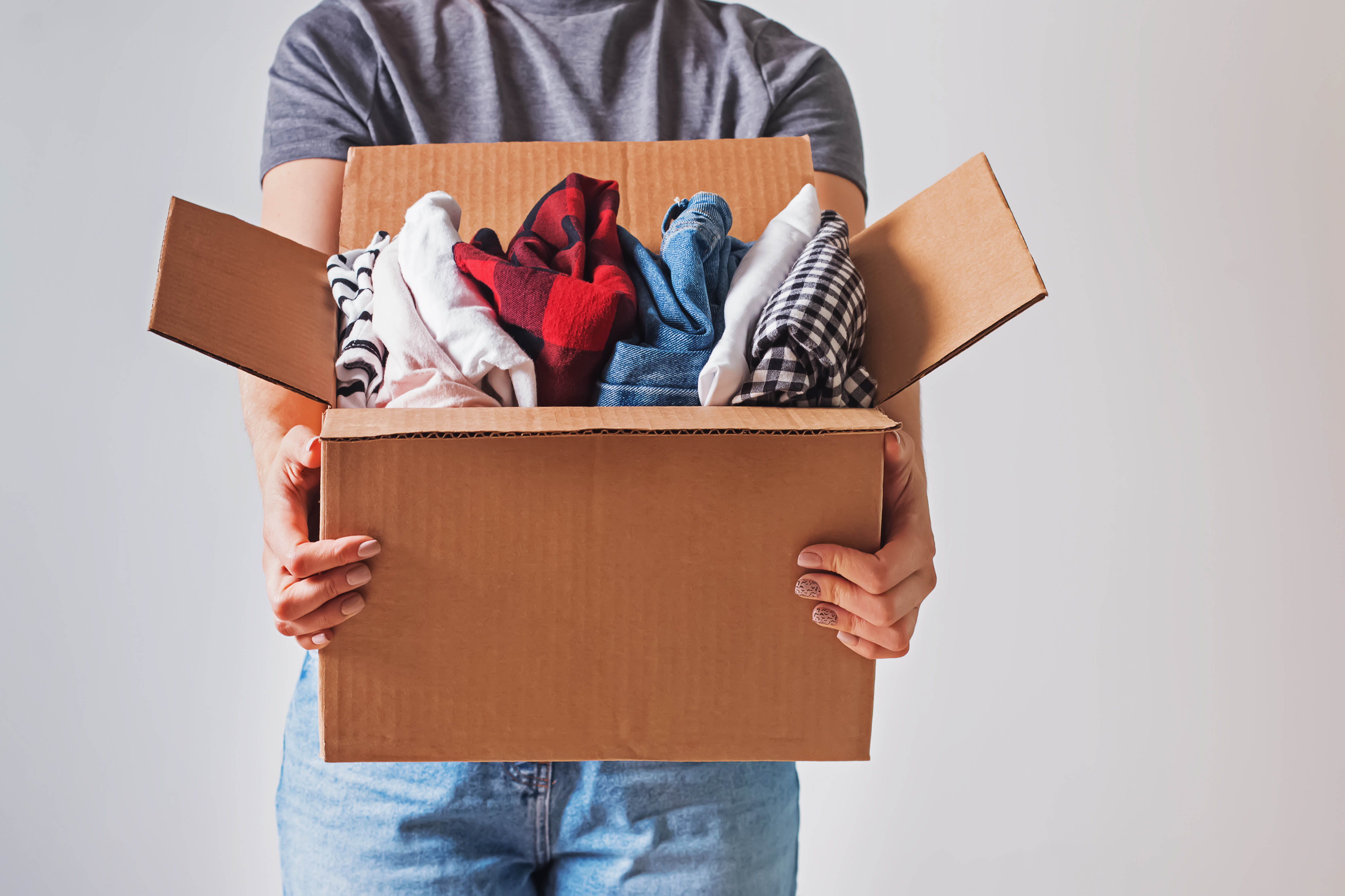 A person holding a cardboard box full of clothing.