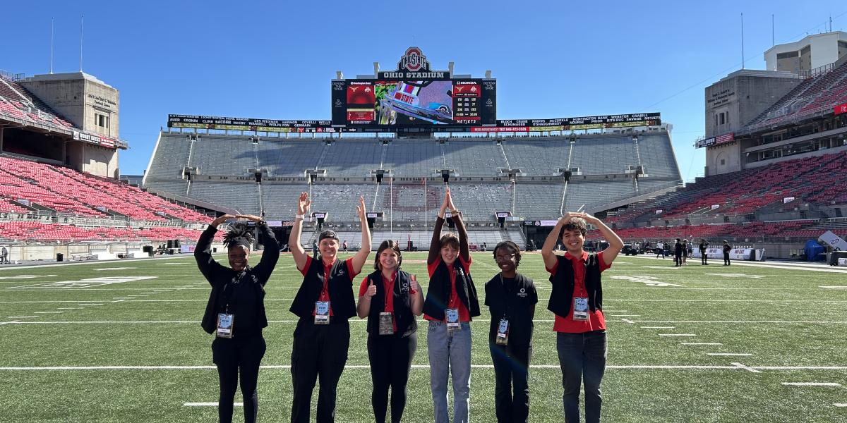 Six student interns spell out O-H-I-O with their arms while standing inside Ohio Stadium.