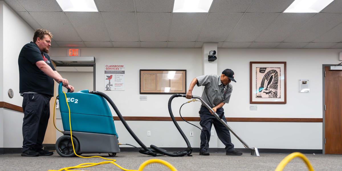 Two men are seen cleaning a carpet.