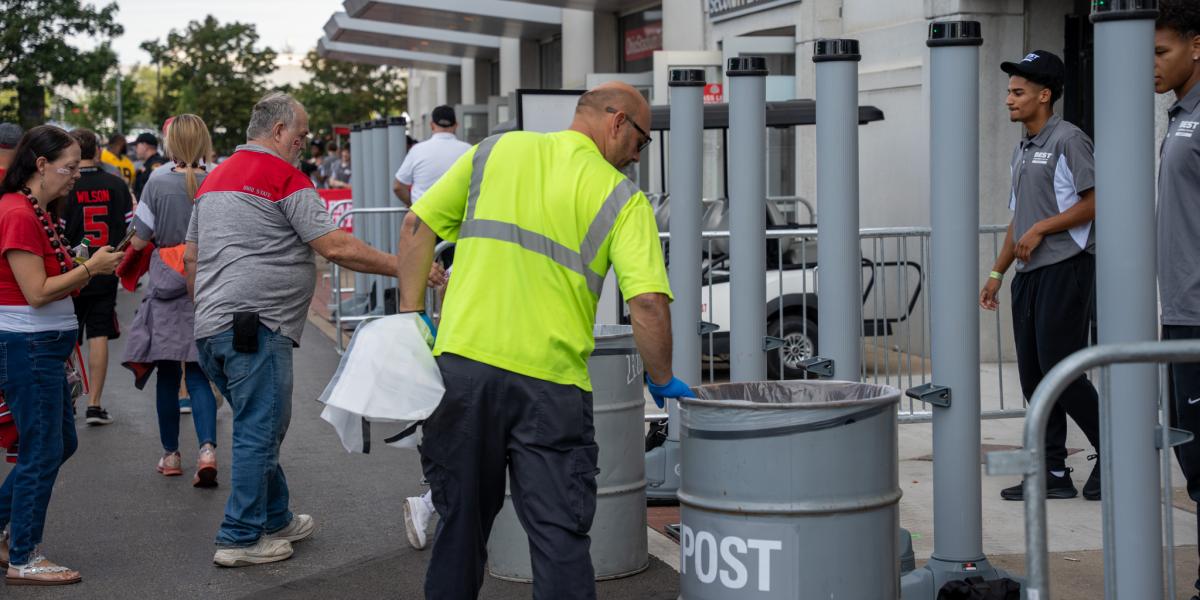 A man wearing a high visibility vest checking a trash bin.