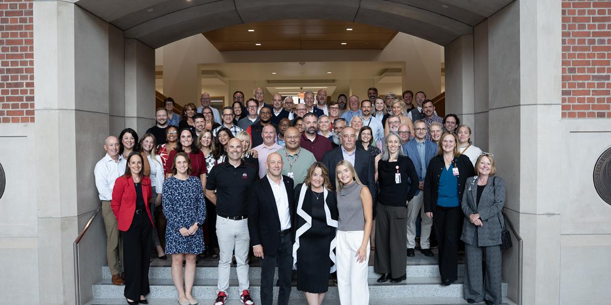 A group shot of everyone smiling at the retirement party. Mark, his wife and daughter are at the front of the group.