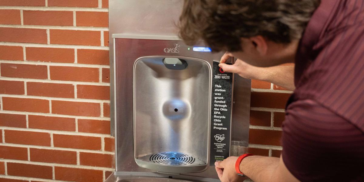 A view of a man putting a sticker on the side of a water bottle refill station.