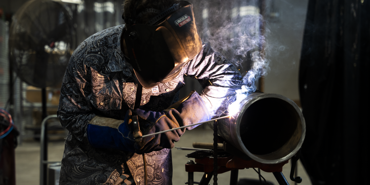 A welding student is seen welding a large pipe.