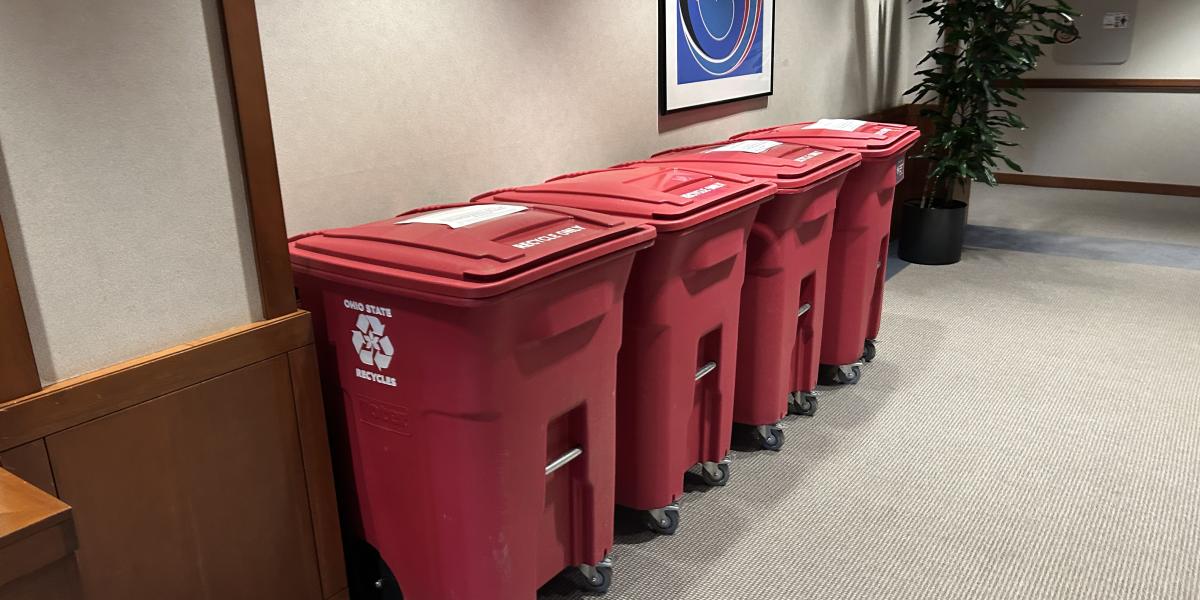Four red recycle bins lined up against a wall