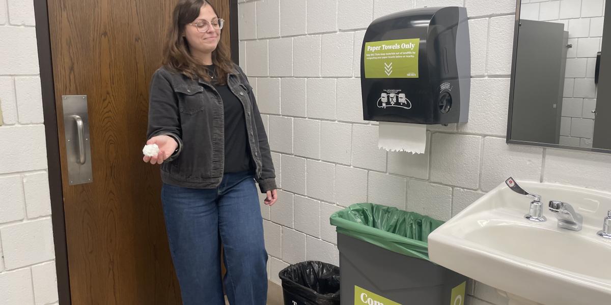 A woman is seen about to put a paper towel into a paper towel specific compost bin.