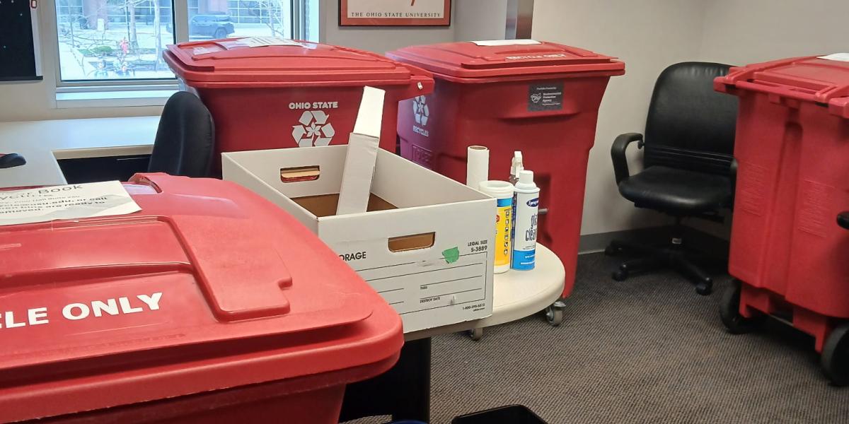 An office with four red recycling bins and cleaning supplies.
