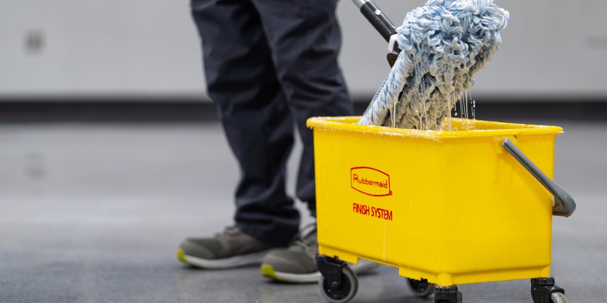 A view of a mop coming out of a large yellow mop bucket. 