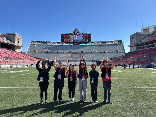 Six student interns spell out O-H-I-O with their arms while standing inside Ohio Stadium.