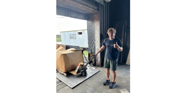A view of Logan Gould holding a thumbs up while holding a handle of a bin of recyclable materials.