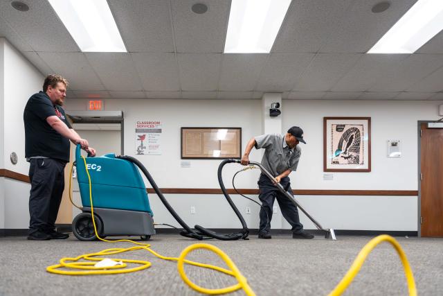 Two men are seen cleaning a carpet.