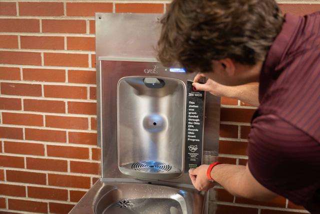 A view of a man putting a sticker on the side of a water bottle refill station.