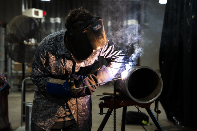 A welding student is seen welding a large pipe.