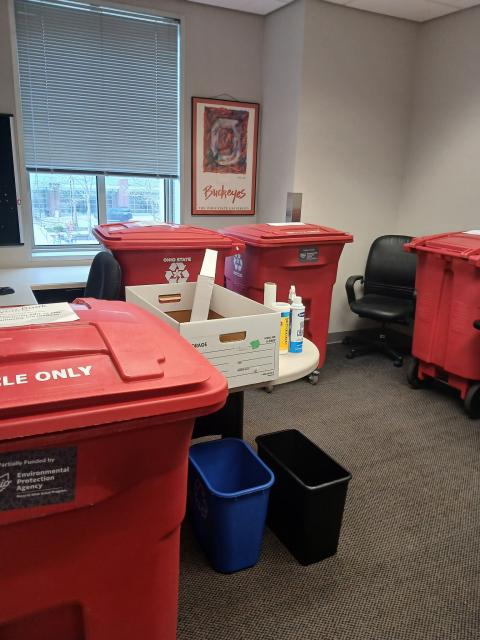 An office with four red recycling bins and cleaning supplies.