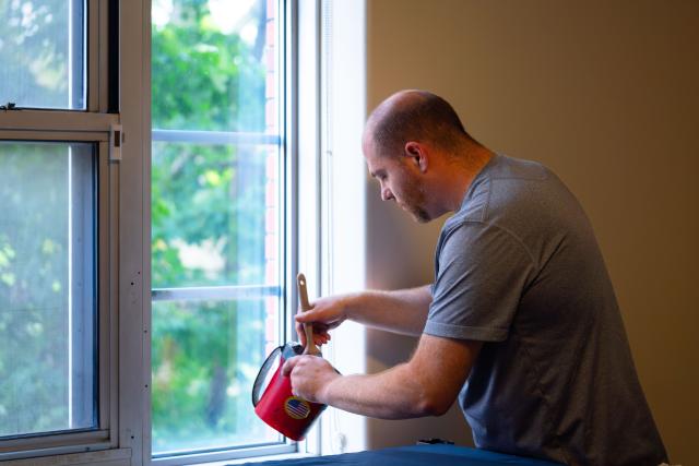 A man painting right next to a window