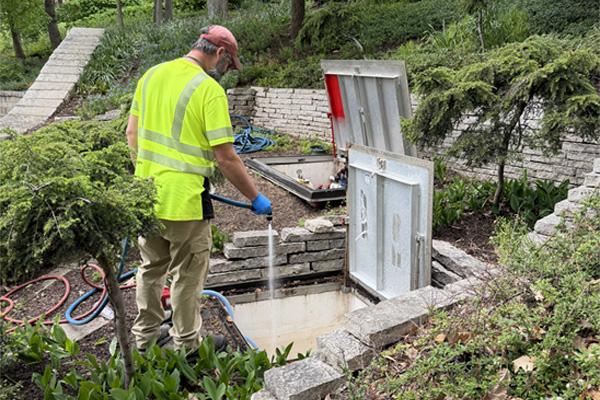 A man wearing a yellow vest using a hose to spray out an in ground storage.
