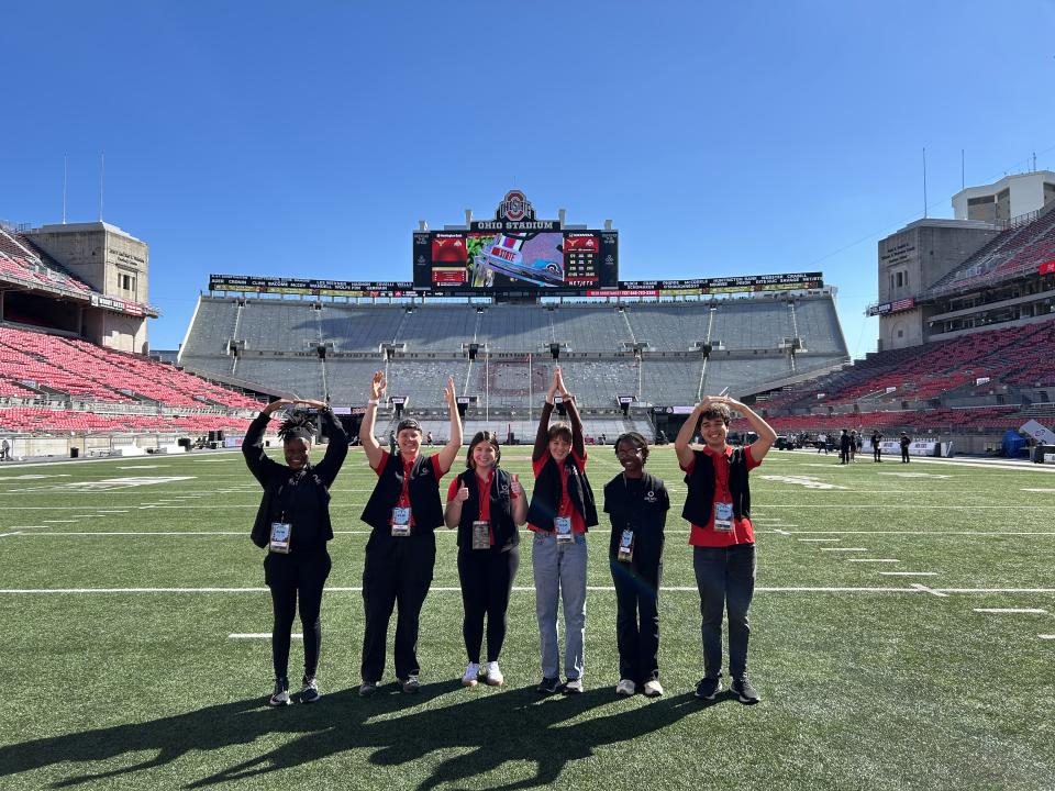 Six student interns spell out O-H-I-O with their arms while standing inside Ohio Stadium.