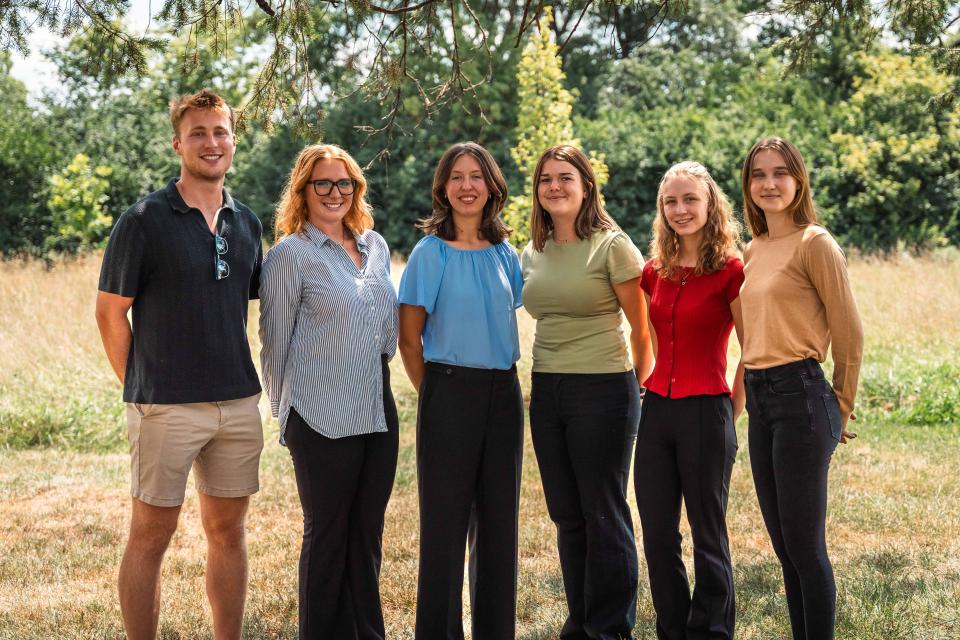 Six interns stand, smiling for a photo outside.
