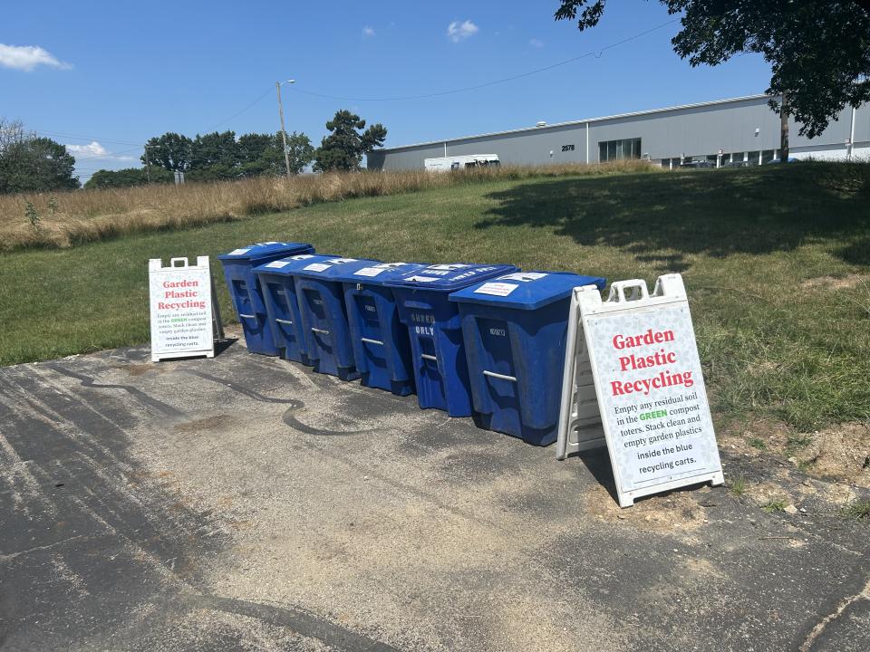 Six blue recycling bins are seen with an A-frame sign on each side about recycling.