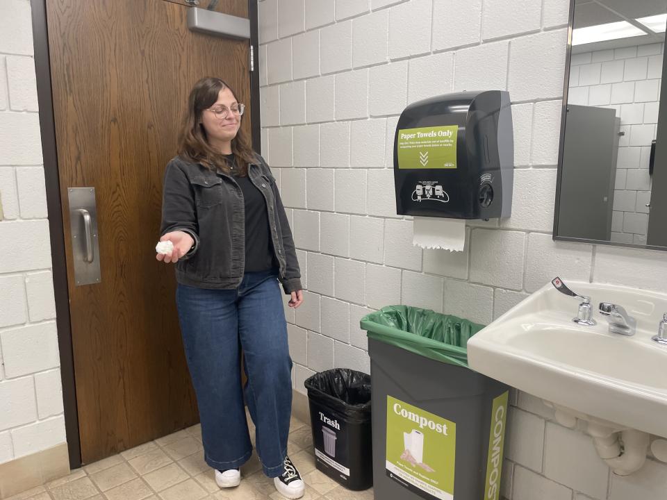 A woman is seen about to put a paper towel into a paper towel specific compost bin.