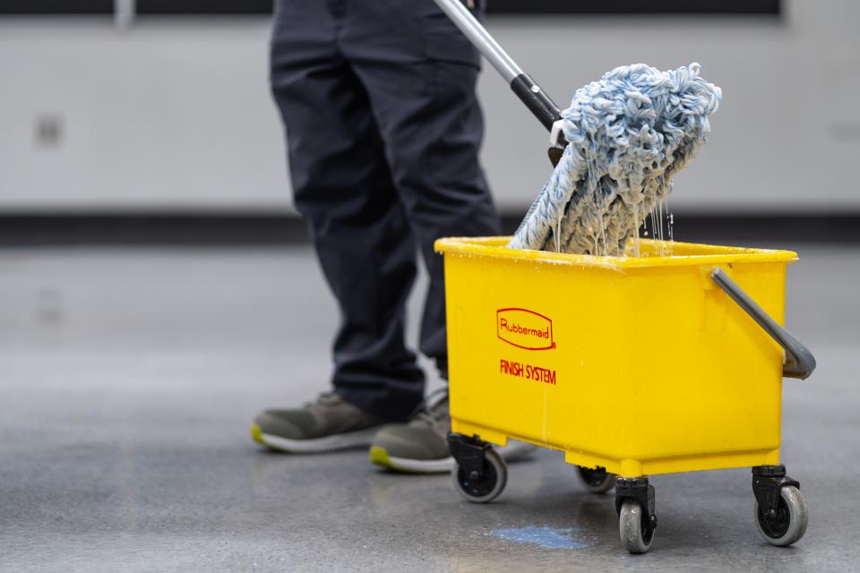 A view of a mop coming out of a large yellow mop bucket.