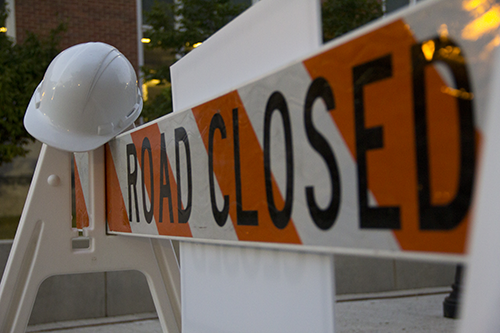 A road closed sign with a hard hat handing from it.